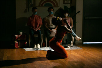 A woman performs in front of audience members wearing masks.