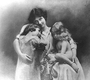 A black and white photo of a mother embracing two children.