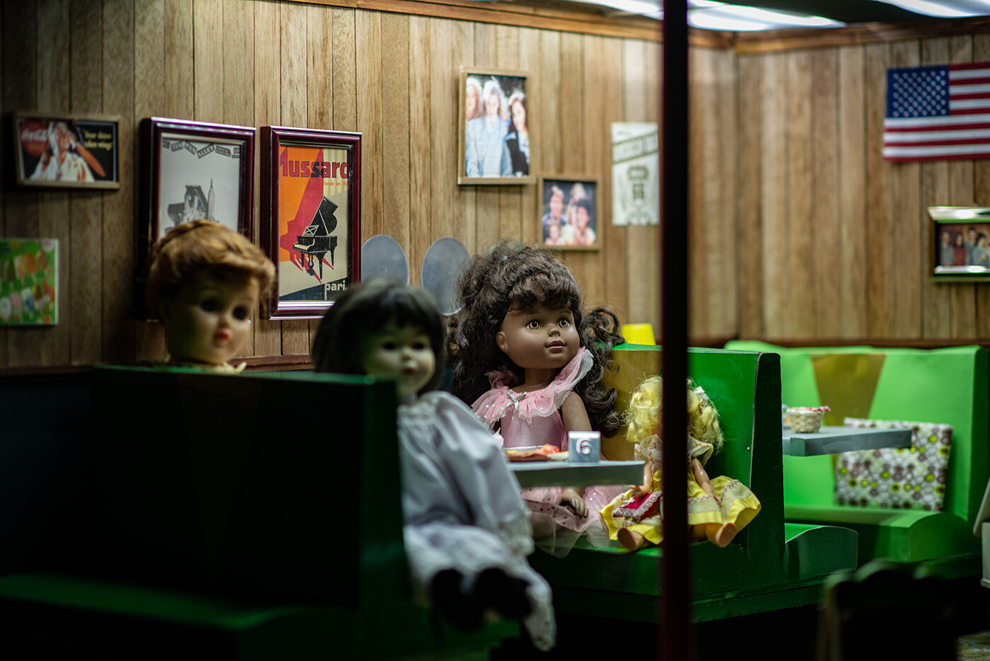A group of dolls sit at a dimly lit restaurant booth.